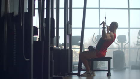 fit man working out on lat pull down machine at the gym. young fit man working out on lat pull down machine at the gym. athletic male uses a lat pull-down machine sitting back to the camera. this exercise builds the back muscles lats biceps and shoulders