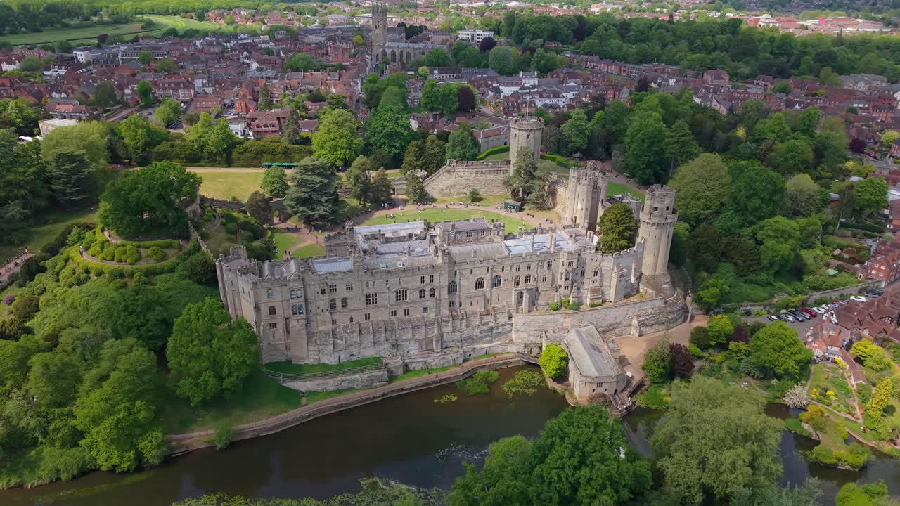 Zoom arrière aérien par drone révélant le donjon du château de Warwick et la ville historique environnante de Warwick par une journée ensoleillée et lumineuse, présentant l'architecture médiévale et le paysage verdoyant