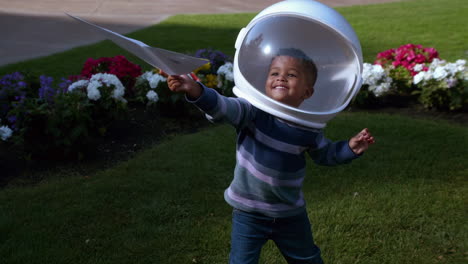a young boy in an astronaut helmet plays with a paper airplane outdoors