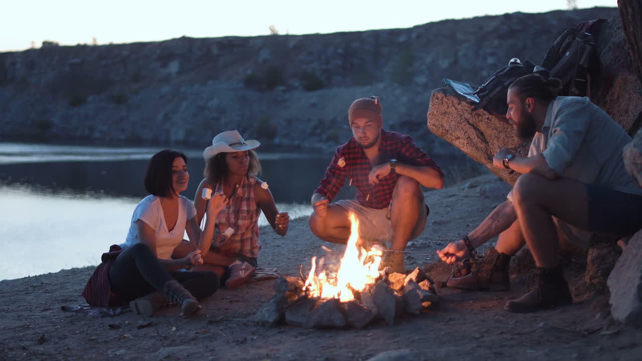 Friends camping by a lake with a campfire