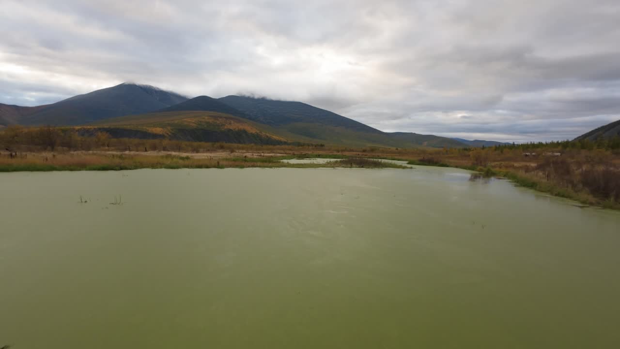 el dron se eleva sobre un estanque tranquilo que refleja el paisaje montañoso, mostrando los hermosos colores de otoño que llenan el paisaje