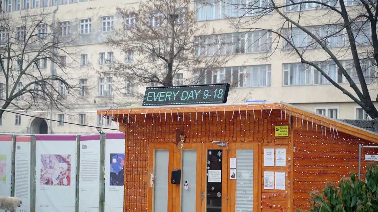 Small wooden COVID test booth with a digital sign and festive lights outside