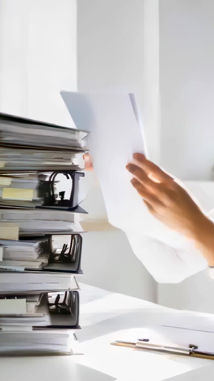 Vertical video: Reaching from right, hands adjusting papers on office desk with binders for filing