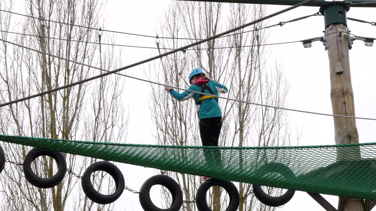 Young girl walking across tyres on ropes on a high wire adventure obstacle course