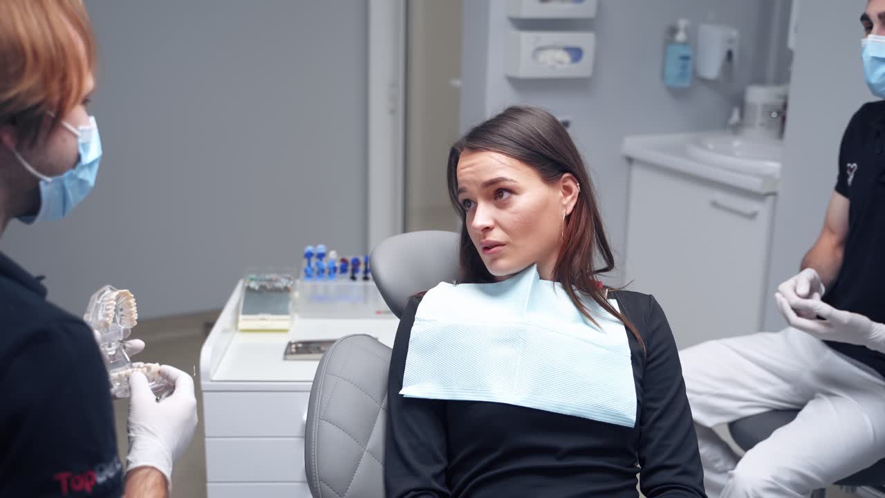 Pretty woman talking to a stomatololist. Male dentist showing artificial jaw to a patient at the dental office. Dental concept.