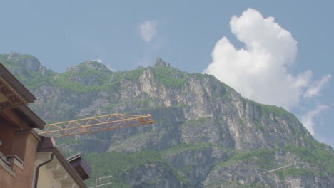 beautiful mountain panorama of the italian alps in riva del garda with a yellow crane and a fluffy white cloud behind the mountain