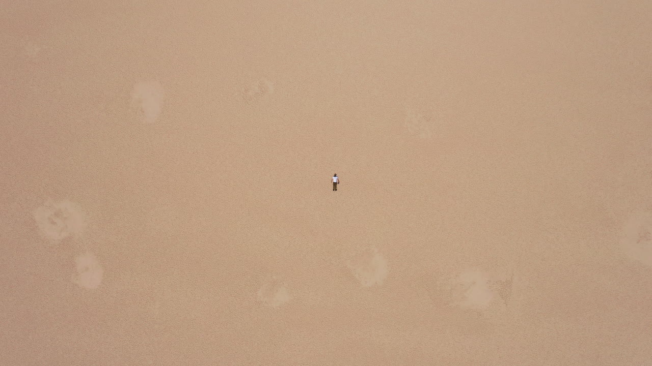 Top down drone shot of a man lying flat on the dry, cracked earth of Deadvlei, Sossusvlei, Namibia