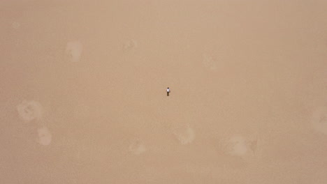 top down drone shot of a man lying flat on the dry, cracked earth of deadvlei, sossusvlei, namibia