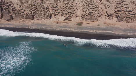 aerial: two children swim in shallow water with big waves in vlychada beach of santorini, 4k prores