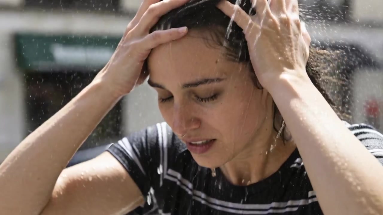 Receiving strong stream of water, woman rinsing and rubbing hair on sidewalk with striped shirt