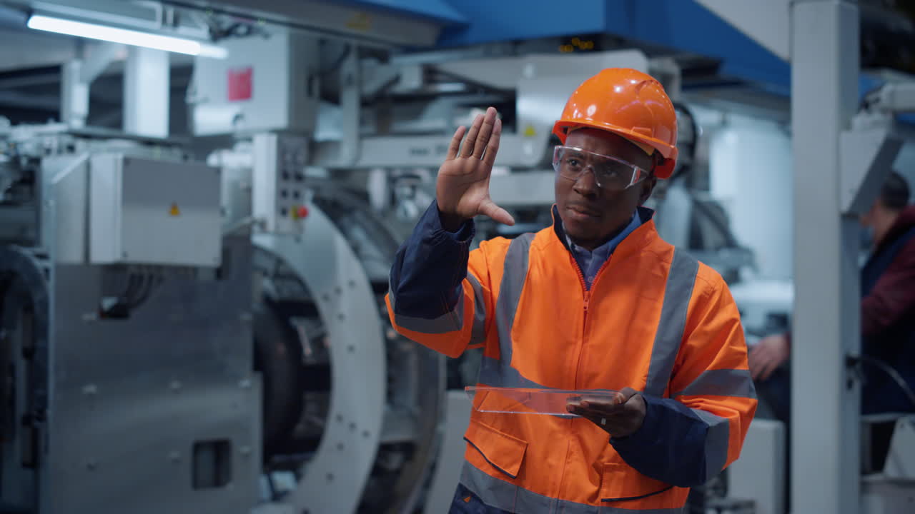 Uniformed specialist working transparent tablet at factory. Analyst work concept