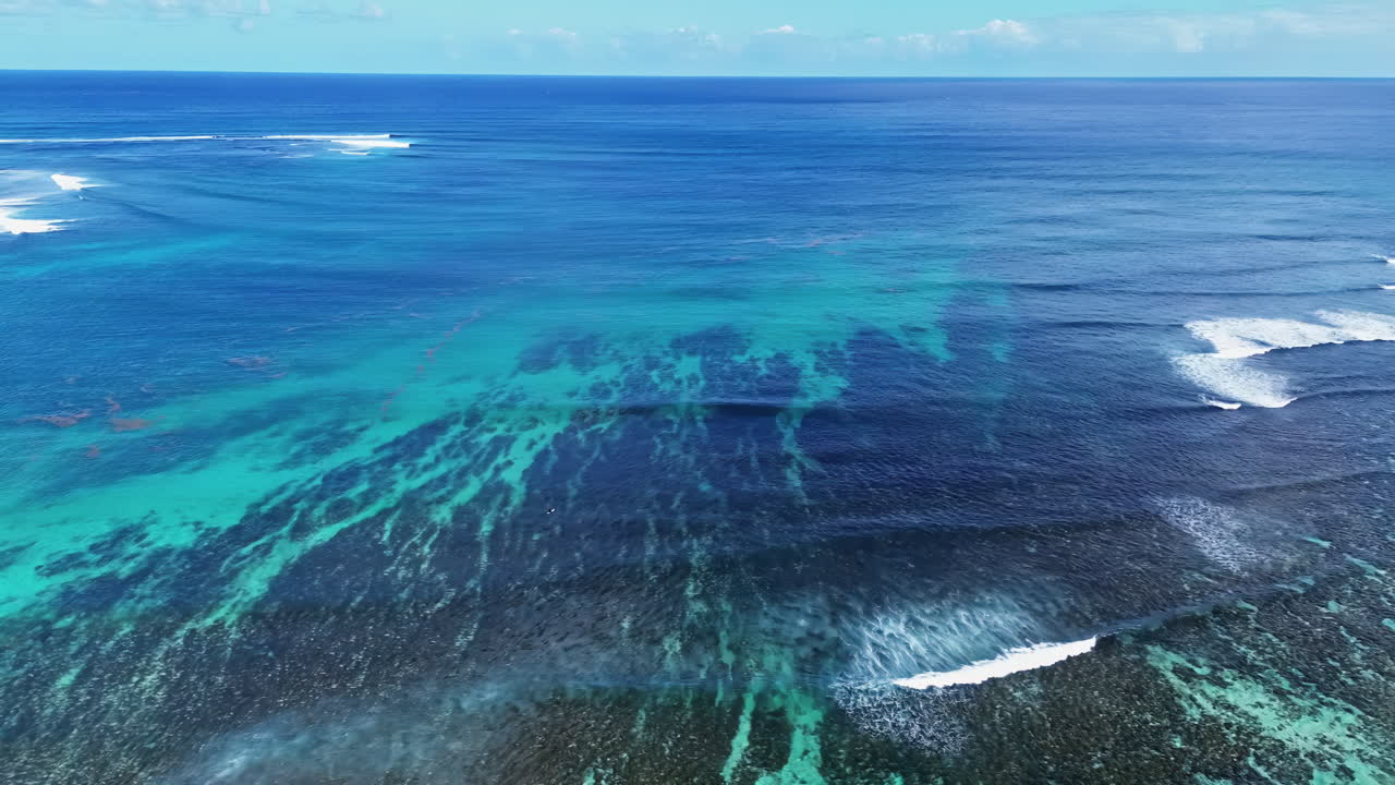 Vue aérienne par drone capturant les vagues se brisant le long d'un récif corallien avec des eaux turquoise vibrantes du lagon, présentant le paysage marin tropical de l'île Maurice.