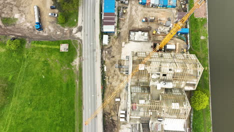 aerial view of a construction site with a crane next to a road, flanked by a green field and industrial containers