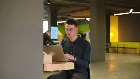 sexy attractive male wearing glasses typing something on laptop. working process in open co-working space. slow motion footage.