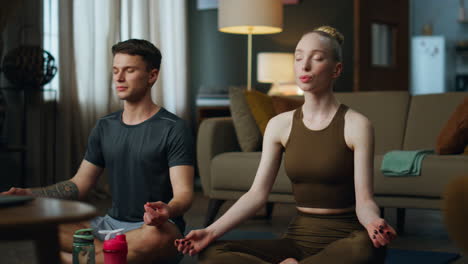 young couple meditating home together. calm pair sitting lotus pose doing yoga.