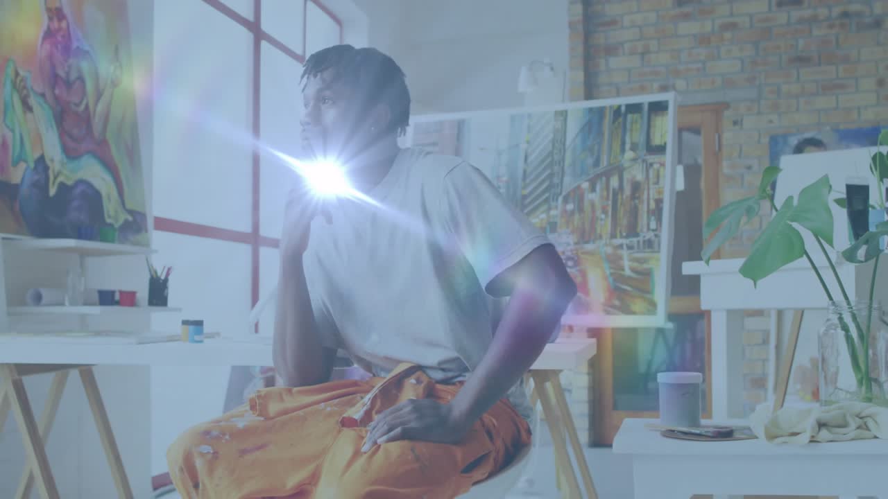 Artist holding chin and watching lens flares drifting across art studio for inspiration