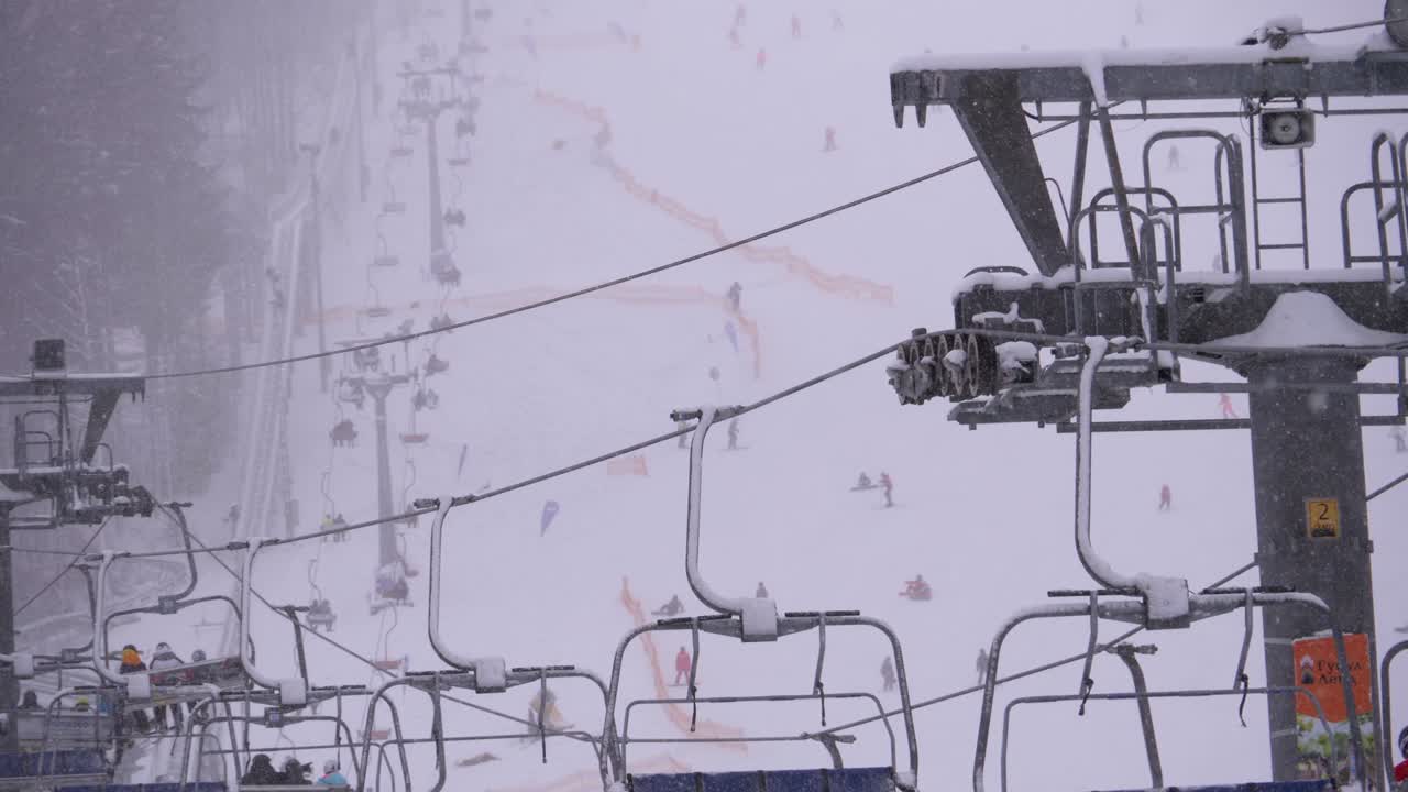 스키 리조트에서 스키 리프트, 느린 모션. 스키 선수들은 스키 의자 엘리베이터를 타고 눈이 내리는 스키 경사에 올라갑니다.