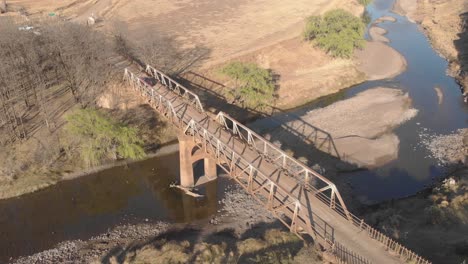 Toma-Aérea-Bloqueada-De-Un-Automóvil-Que-Cruza-Un-Viejo-Puente-De-Acero