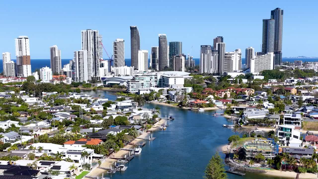 Drone glides above river, suburban homes, and high-rise skyline under bright midday sunlight