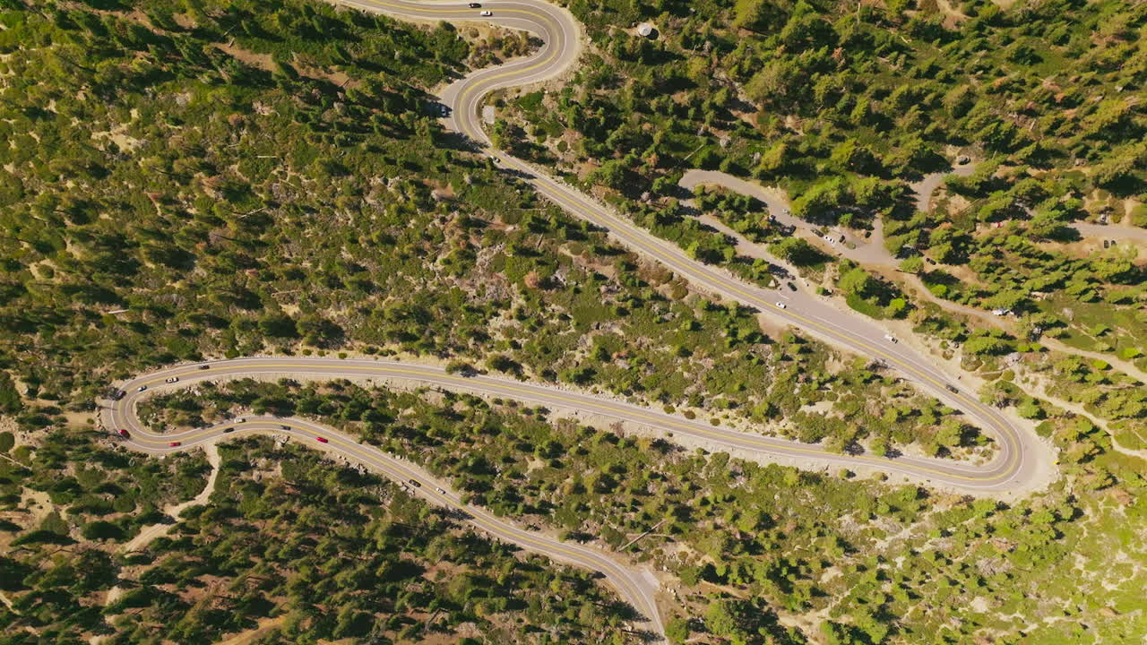 Cars moving leisurely by the winding road going through the green landscape. Drone descending over the highway on sunny daytime.