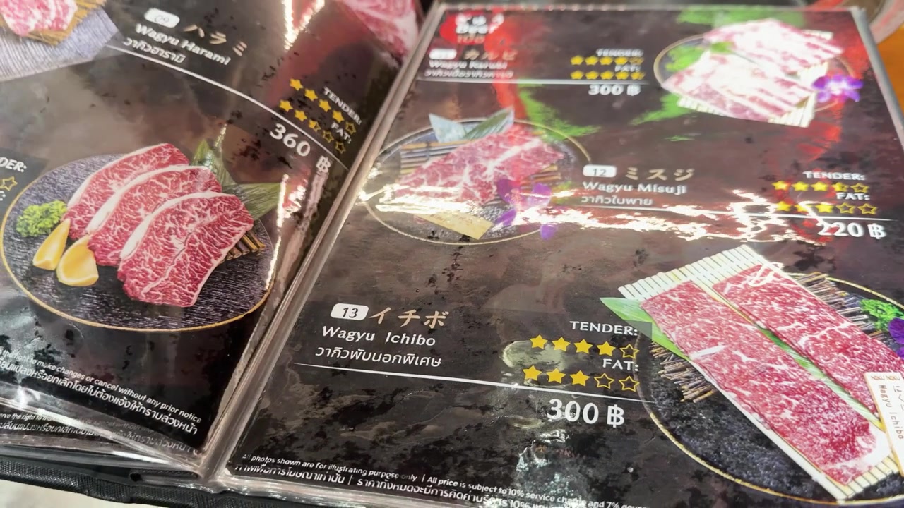 En hånd bladrer igennem en farverig japansk restaurantmenu, der viser forskellige udskæringer af premium Wagyu-oksekød.