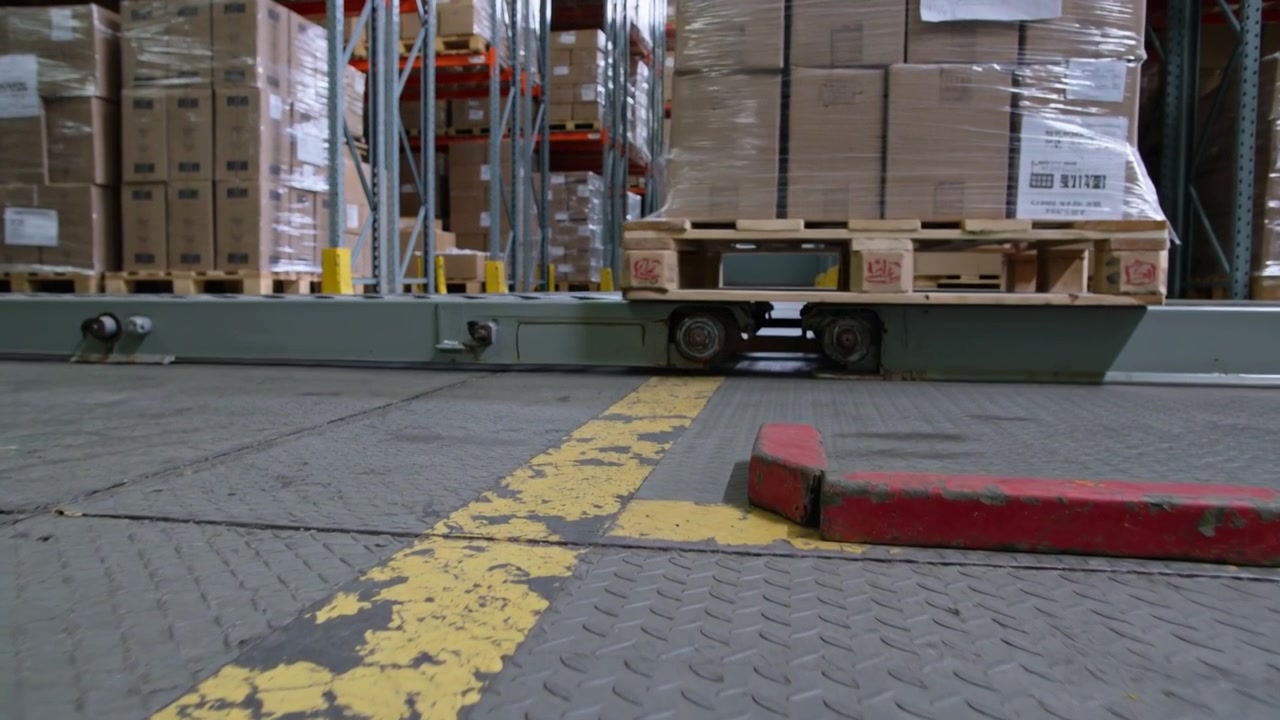 Motore in avviamento, carrello che trasporta scatole imballate su pallet si muove lungo la guida del magazzino per la consegna.