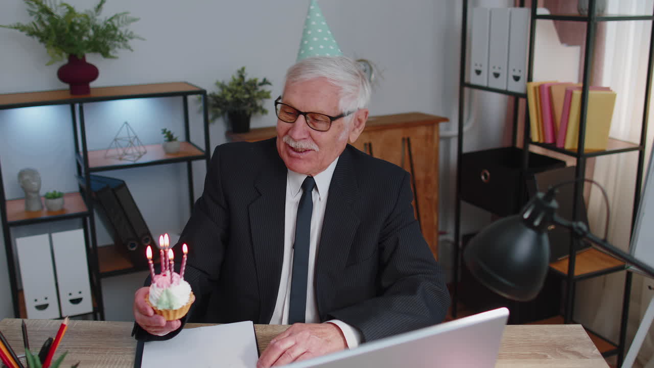 anciano empresario celebrando su cumpleaños en la oficina sosteniendo un pequeño pastel con velas haciendo un deseo