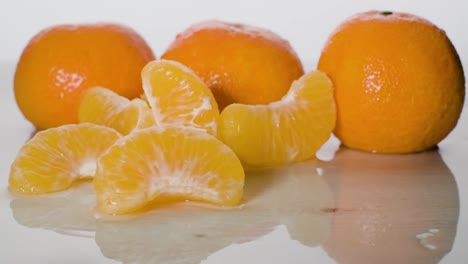 still shot mandarin fruits displayed on wet surface, slice falls on white background