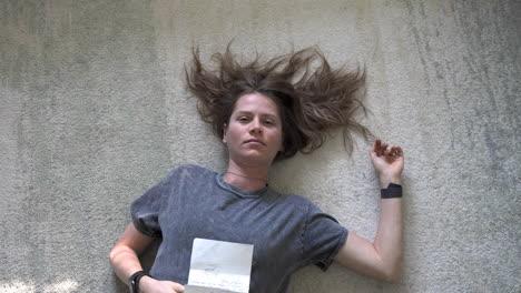 a serene topshot of a woman lying down with a love letter on her stomach, as the camera gently descends and rotates around her.