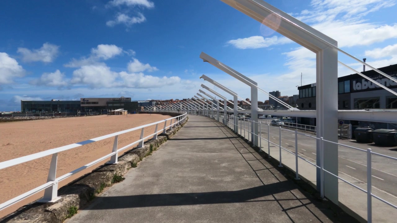 Percorso pedonale pavimentato con archi moderni accanto alla spiaggia di Poniente a Gijón