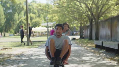 hombre asiático feliz sentado en patineta, hija empujándolo