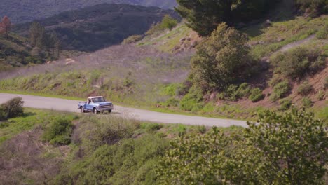 a blue pickup truck drives on a rural road