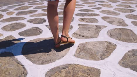 woman tourist in sandals and skirt walking down traditional white painted street found on many greek islands