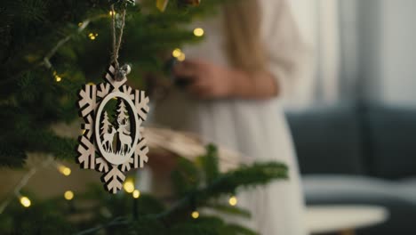 Wooden-pendant-hanging-on-Christmas-tree-and-girl-dressing-the-tree-in-the-background.