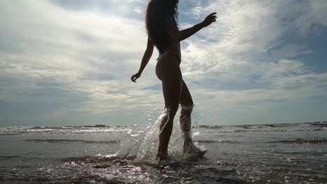 beautiful young woman walks on beach and splashes in sea on holiday