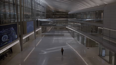 a lone figure walks through a vast, modern architectural interior
