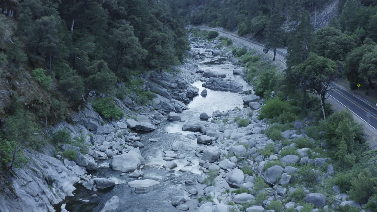 Riprese aeree in avanti attraverso una gola forestale con il fiume sottostante e alberi ai lati.