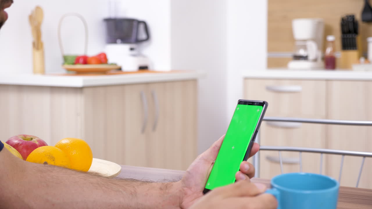 Man using smartphone with green screen in kitchen
