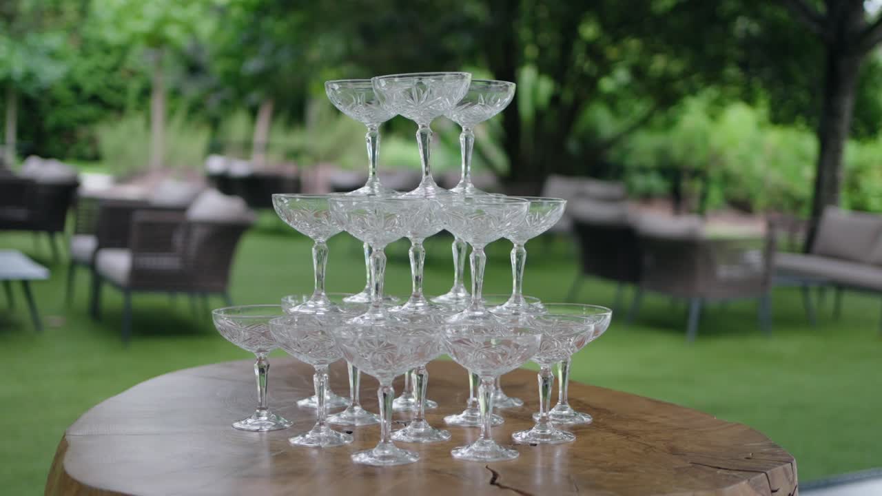 Empty champagne glasses stacked in a pyramid on a wooden table outdoors.