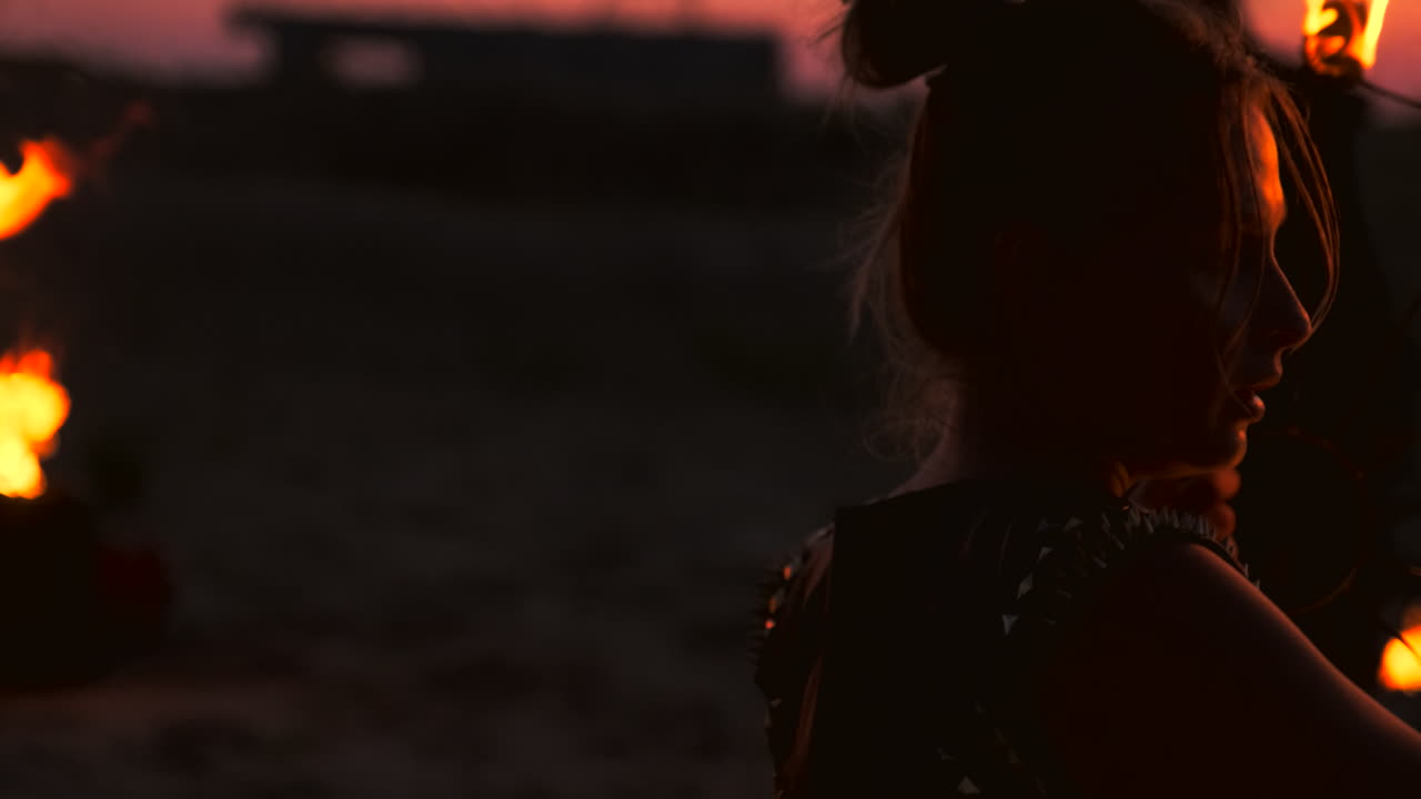 un grupo de hombres y mujeres muestran fuego por la noche en la arena contra el fondo de fuego y grúas de la torre.