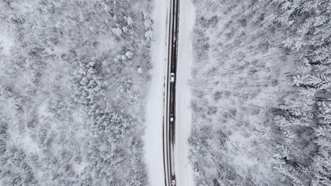 Four-cars-driving-on-snowy-winter-road,-drone-camera-facing-down