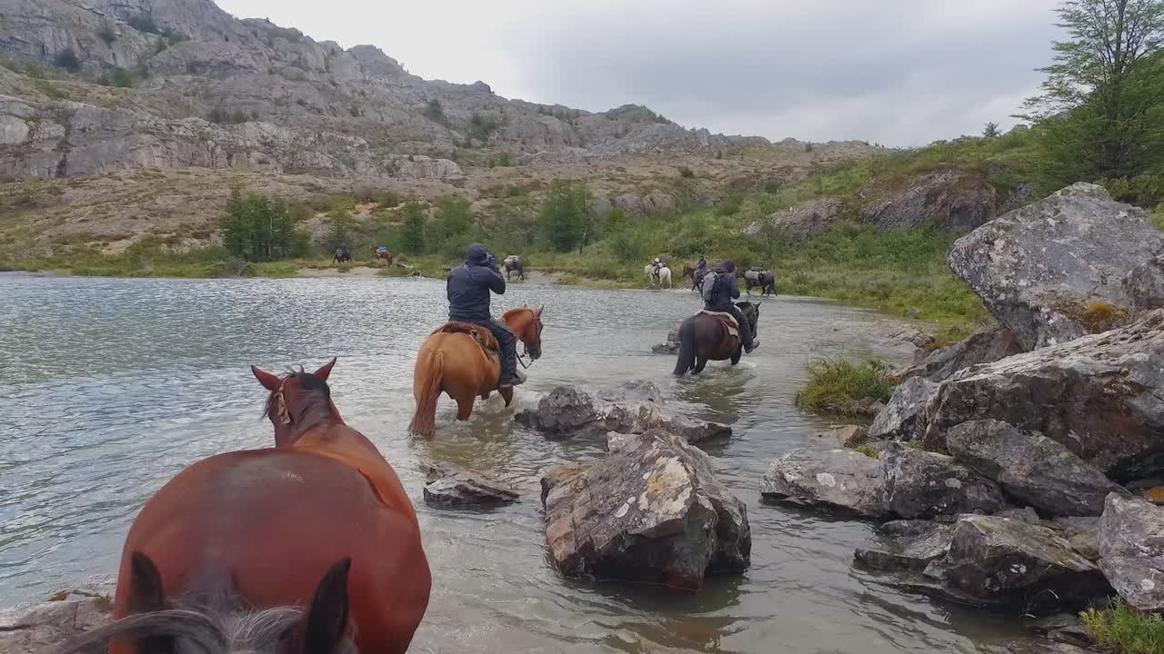 말을 탄 사람들은 강을 따라 다른 말들을 끌고 간다