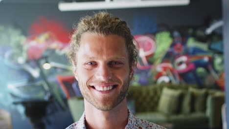 young white man in front of mural in workplace smiling to camera and laughing, head shot