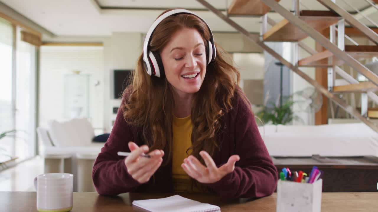 Caucasian woman sitting at desk wearing headphones having video call smiling