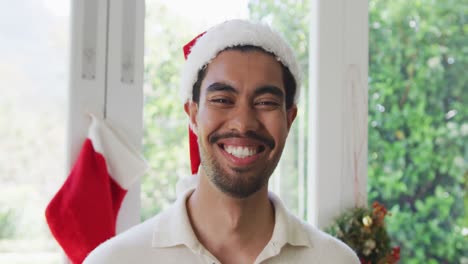 retrato de un joven biracial feliz con sombrero de santa en casa durante la navidad