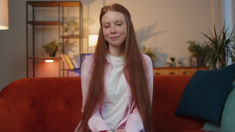 Child-girl-sits-on-home-couch-looking-at-camera-making-video-conference-call-with-friends-or-family