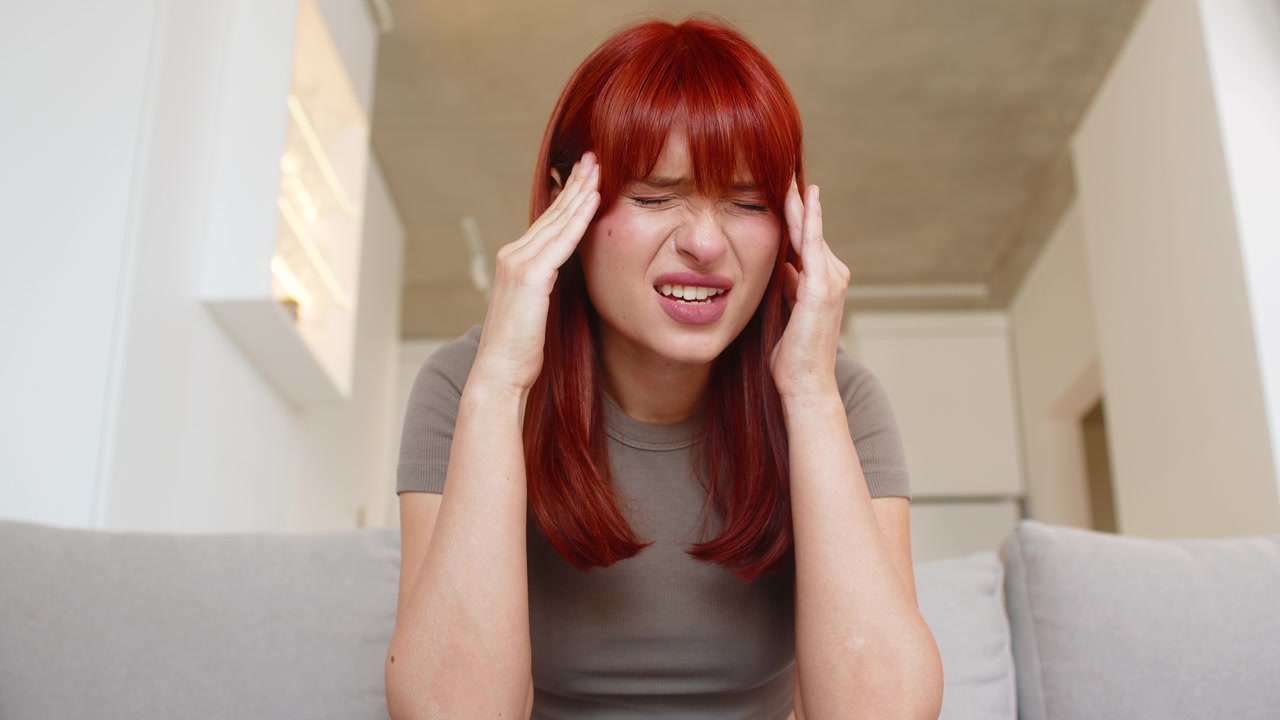 Young woman holds head with strong headache closes eyes rubs temples for relief short pause and rest