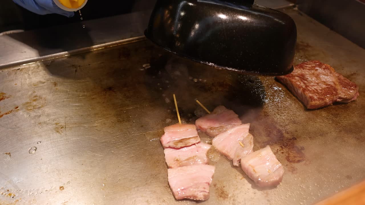 Uno chef di street food condisce e ricopre spiedini di manzo wagyu su una piastra teppanyaki rovente