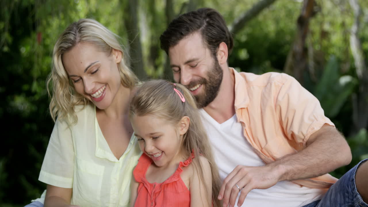 Cute family are sitting on the grass and looking a smartphone
