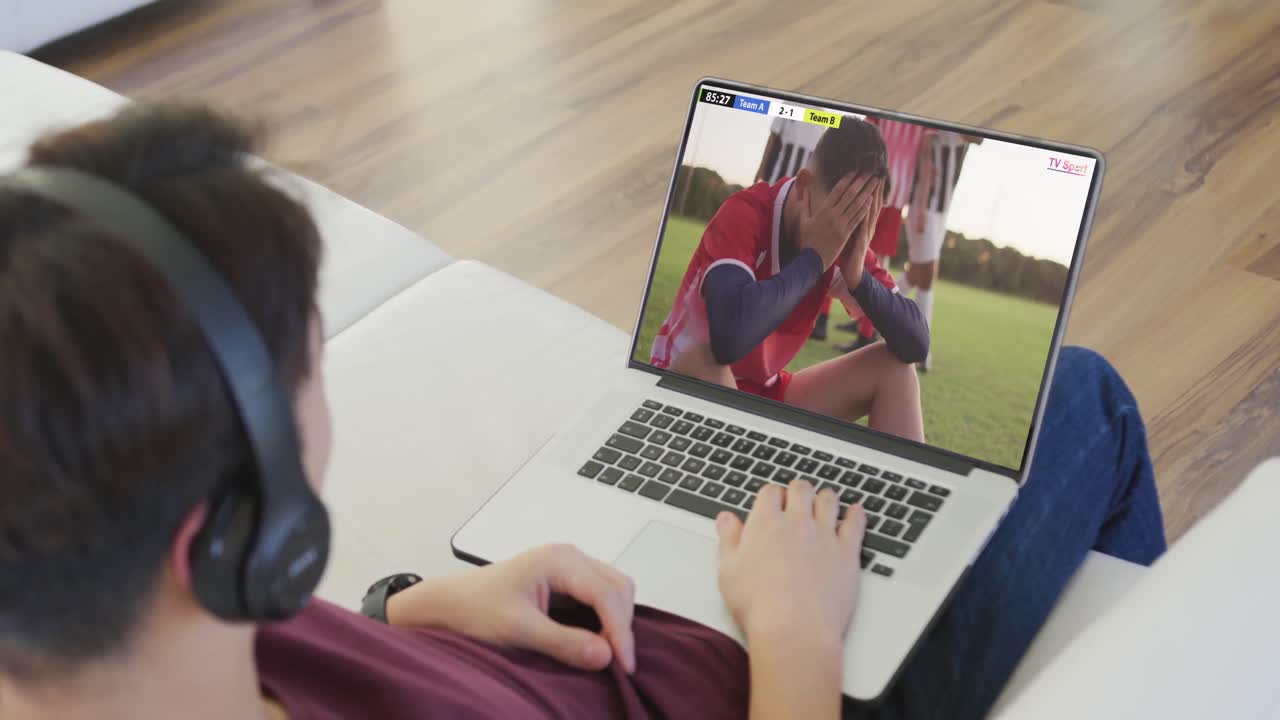 video de una persona sentada en el sofá y viendo un partido de fútbol en una computadora portátil
